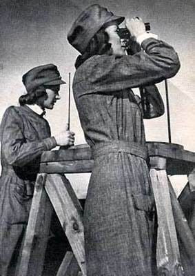 The image shows two people wearing hats and overalls, both using binoculars to look through a wooden structure.
AI-generated content may be incorrect.